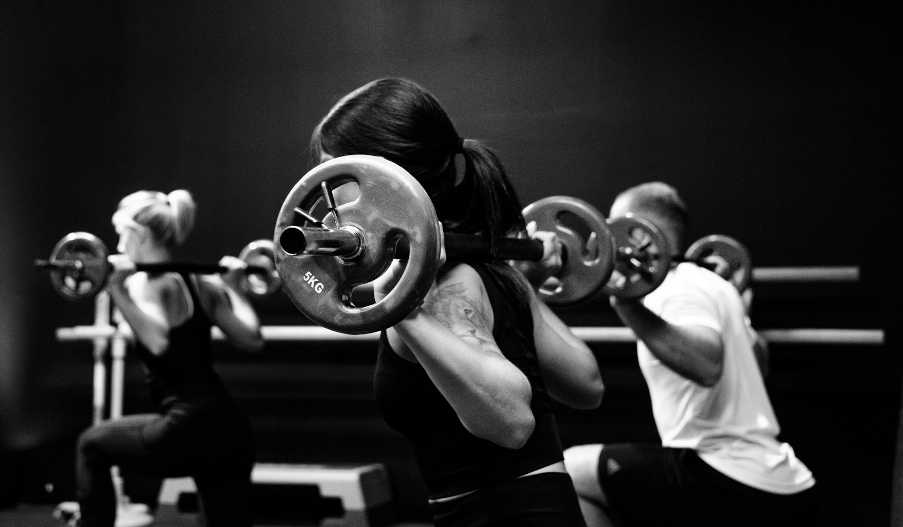 A group class mid-squat, barbells on shoulders, in black and white
