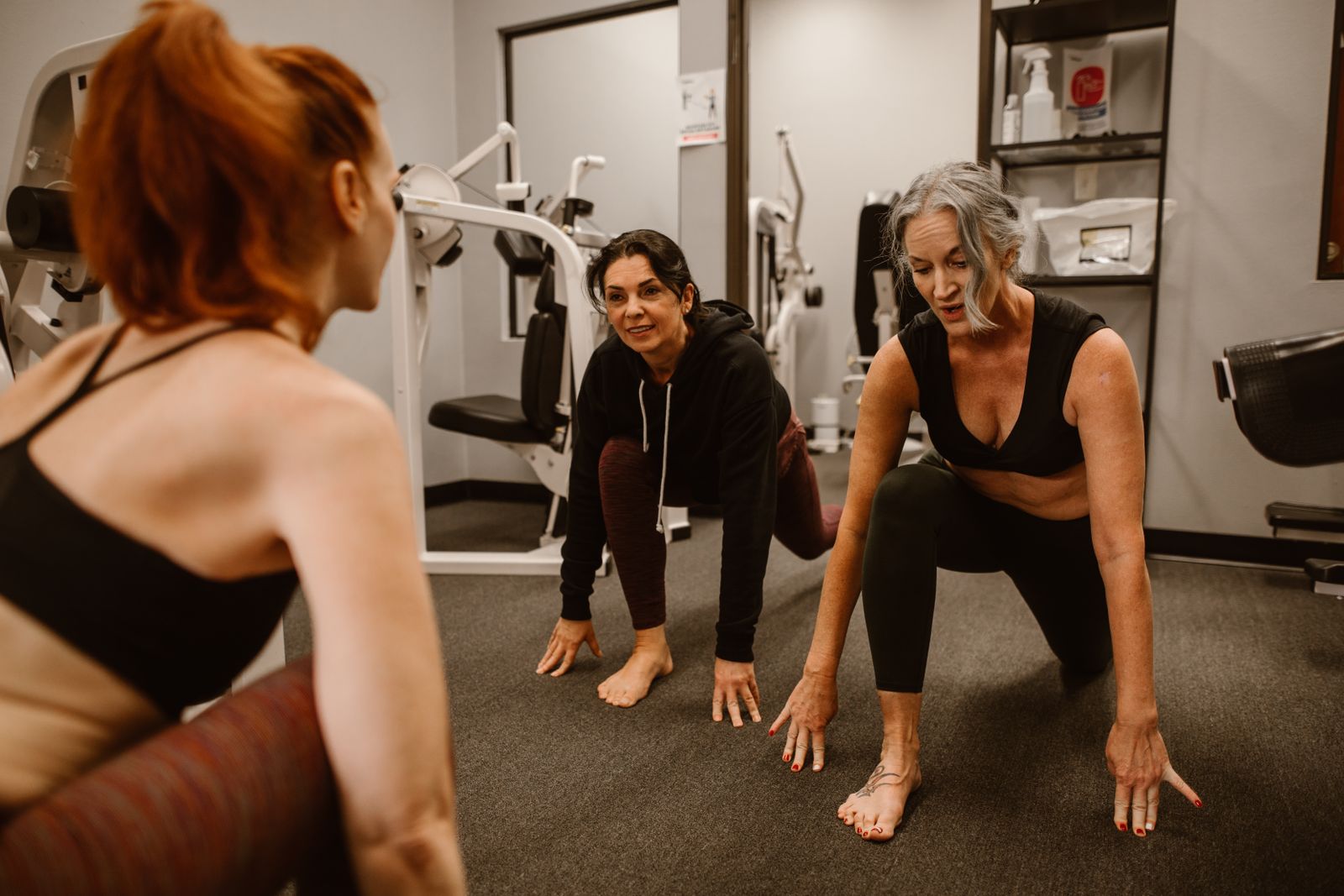 Three women stretching together mid-workout, talking to each other